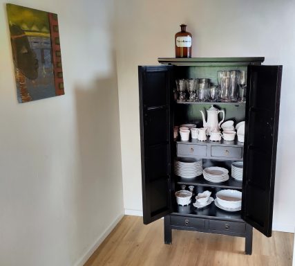 Schwarzer Schrank mit Geschirr und Gläsern, neben einem Bild an der Wand.