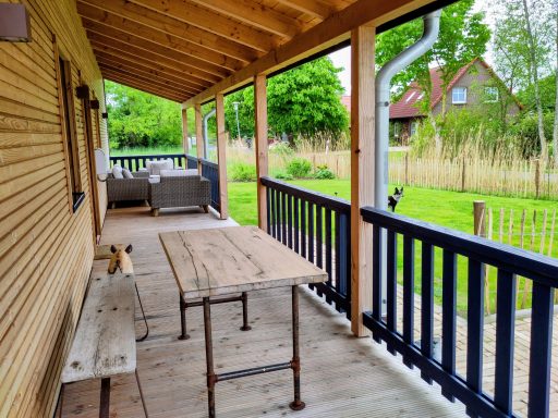 Überdachte Terrasse mit Tisch, Stühlen und Blick auf einen Garten mit Bäumen.