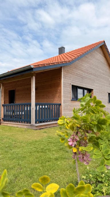 Ein modernes Haus mit rotem Dach und Holzverkleidung, umgeben von grünem Garten.