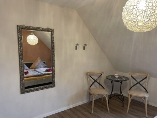 Helles Zimmer mit Spiegel, Tisch und zwei Stühlen, gemütlich dekoriert.