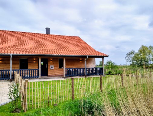 Haus mit rotem Dach, Veranda und umgeben von Gras und Bäumen.