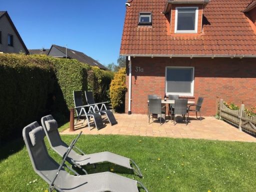 Sonniger Garten mit Liegen, Terrassenmöbeln und einem Backsteinhaus im Hintergrund.
