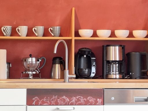 Küchenzeile mit mehreren Kaffeetassen, verschiedenen Kaffeemaschinen und Holzregal.