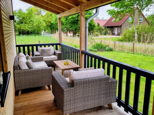 Gemütlicher Balkon mit Möbeln, Blick auf Wiese und Häuser im Hintergrund.