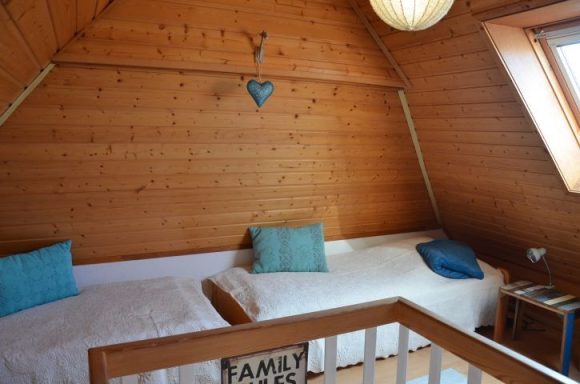 Helles Zimmer mit Holzvertäfelung, zwei Betten und blauen Kissen.