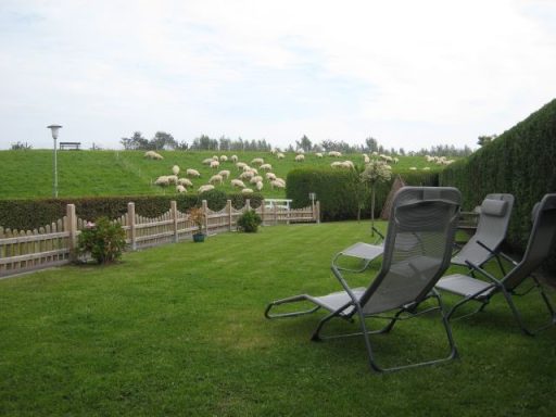 Garten mit Liegen, Hecken und Weinbergen im Hintergrund unter bewölktem Himmel.
