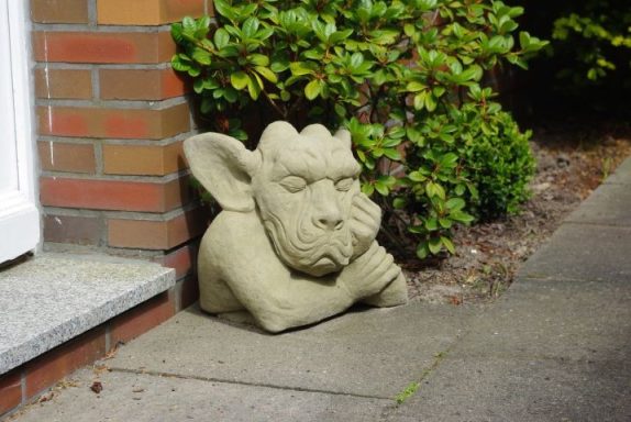 Steinerne Figur eines Fabeltiers mit einem nachdenklichen Ausdruck, an der Wand platziert.