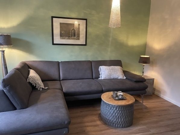 Gemütliche Wohnzimmereinrichtung mit grauem Sofa, Holztisch und grüner Wand.