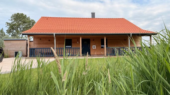 Ein Holzhaus mit rotem Dach, umgeben von hohem Gras und einem klaren Himmel.